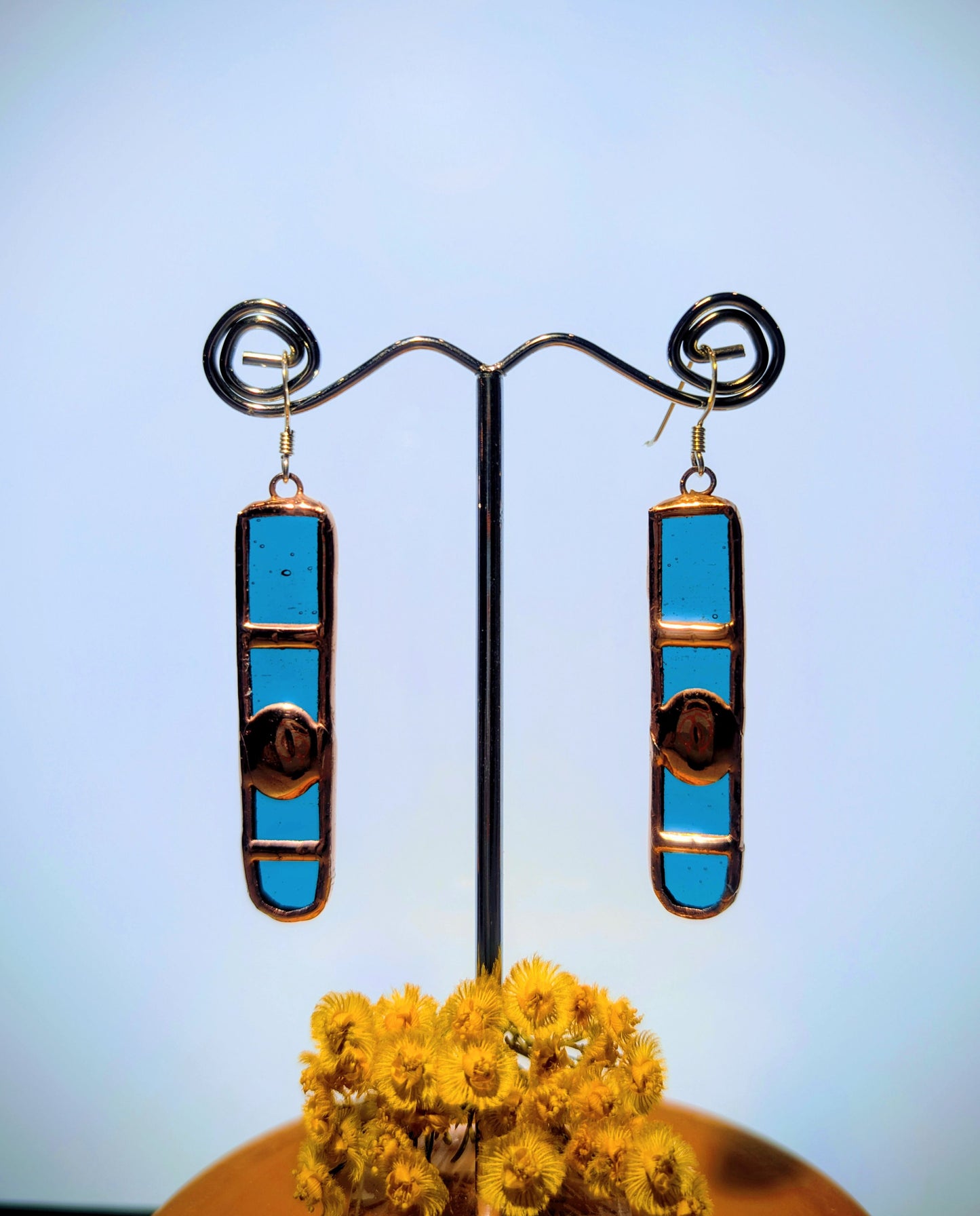 Pair of blue cylindrical earrings on a stand with a blurred background