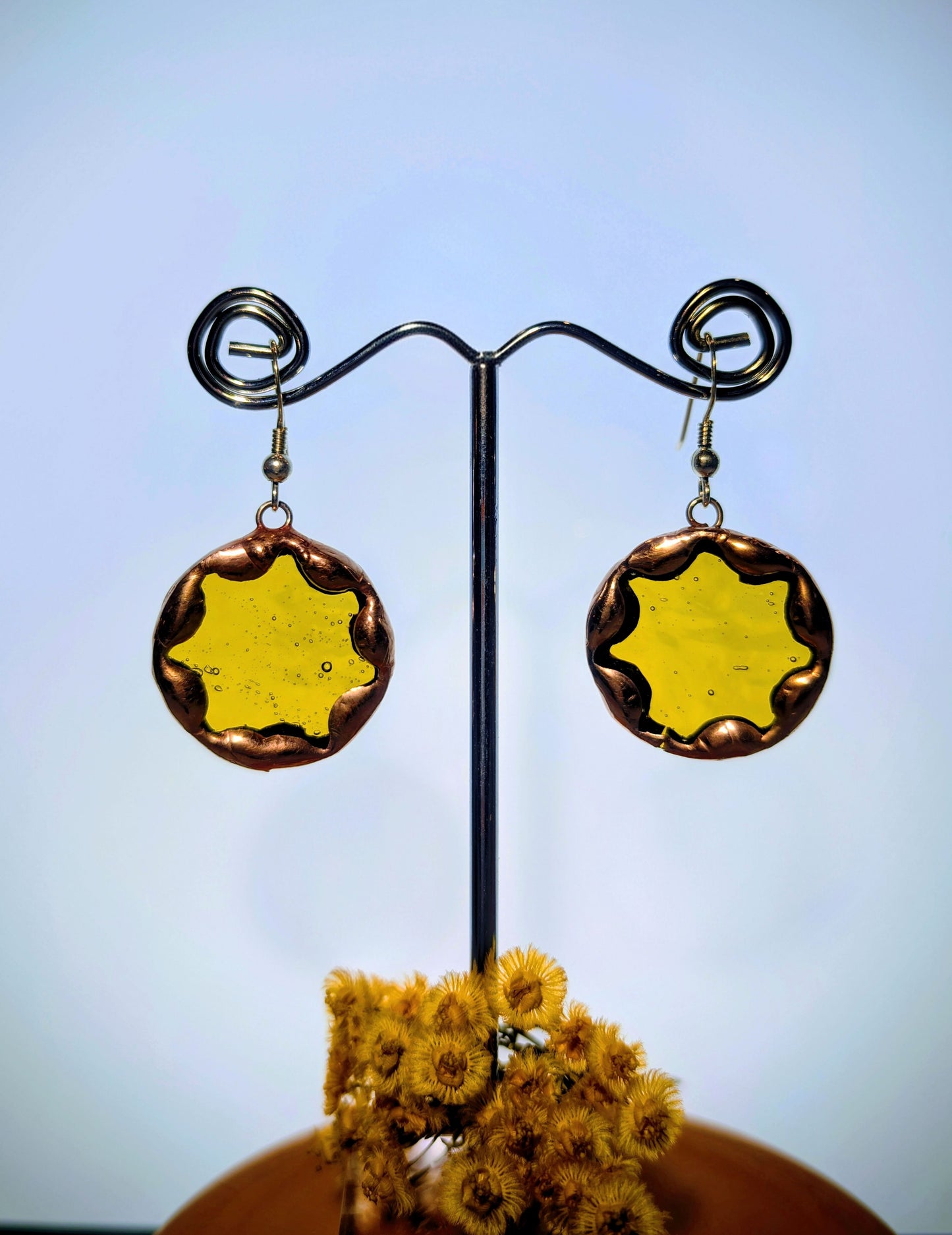 Pair of round earrings with yellow center and brown border on a stand against a blue background.