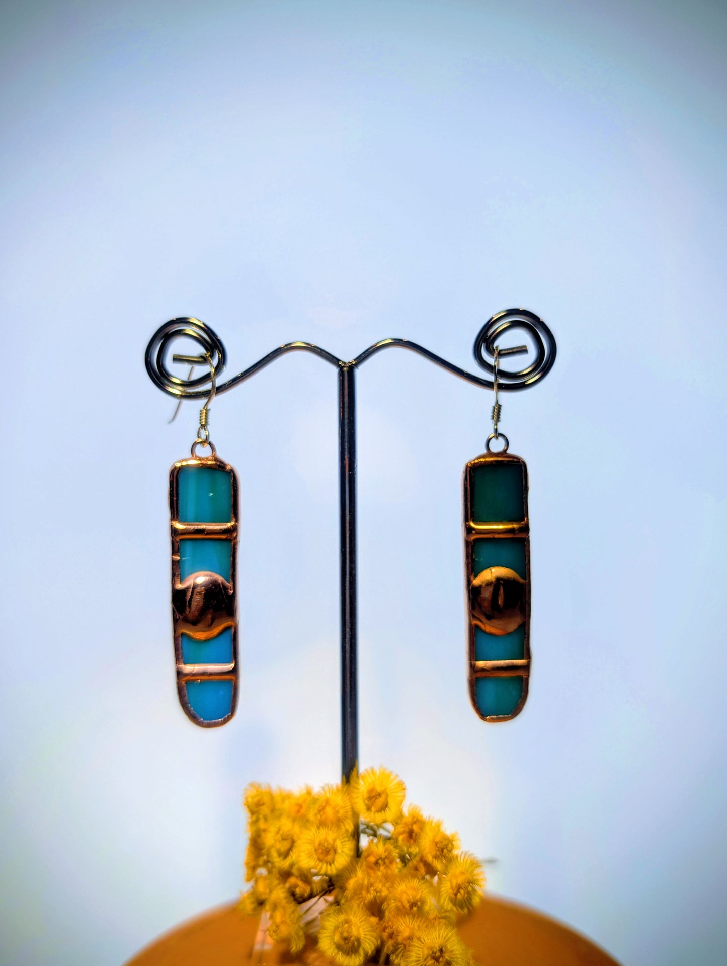 Pair of turquoise and gold earrings on a stand with yellow flowers at the base.