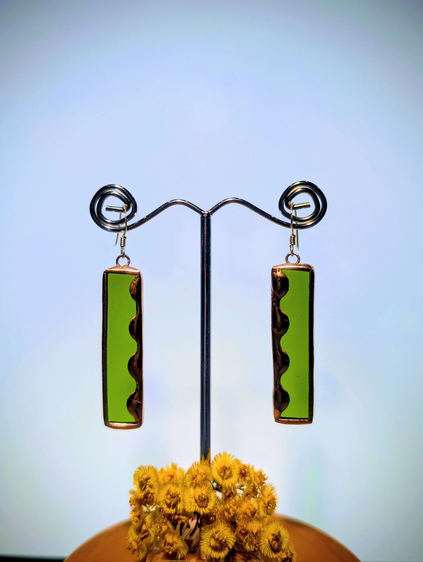 Green and brown rectangular earrings on a stand with a blurred background