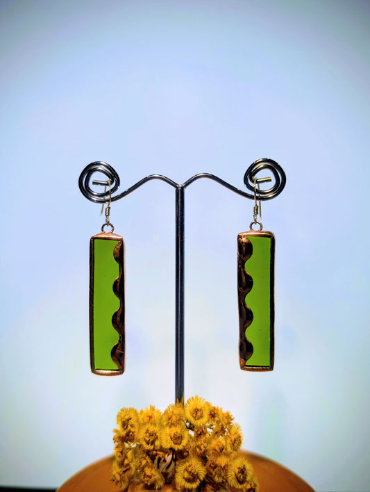 Green and brown rectangular earrings on a stand with a blurred background