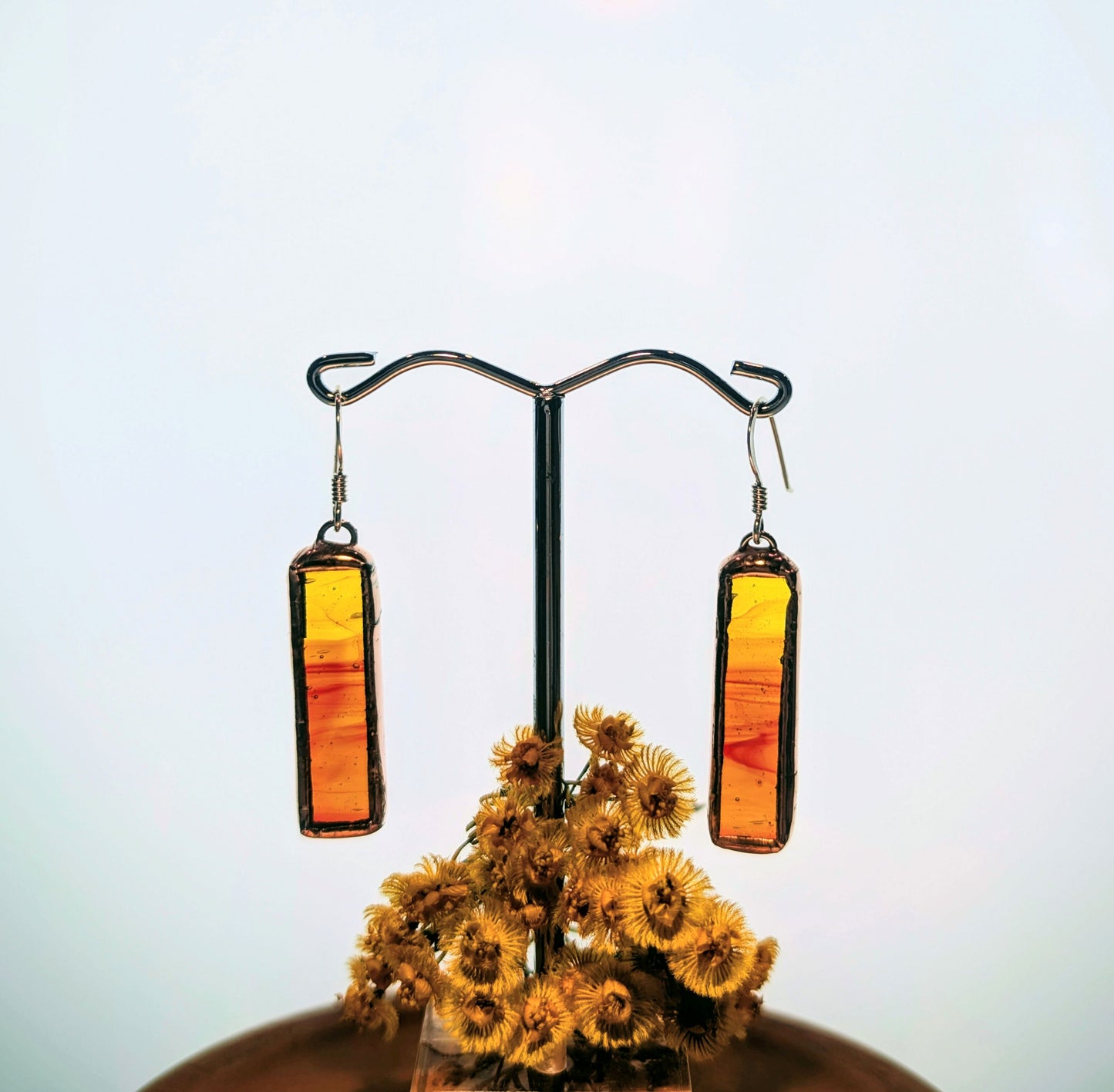Pair of orange and red rectangular earrings on a stand with dried flowers.