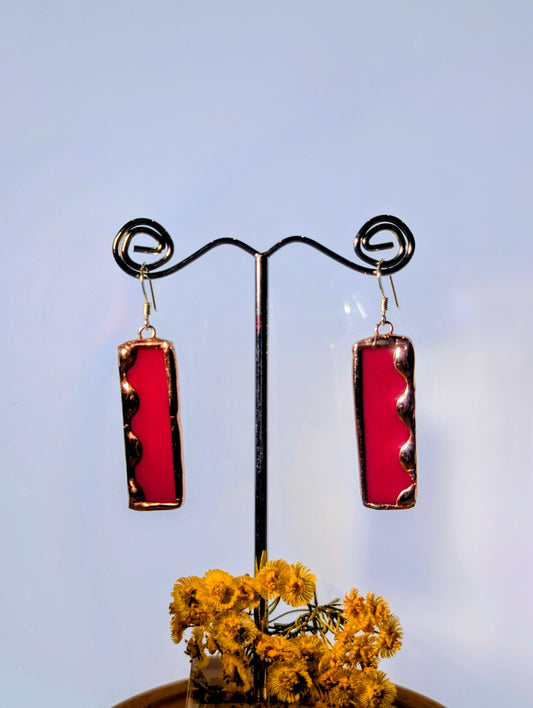 Red rectangular earrings on a black stand with yellow flowers against a light blue background
