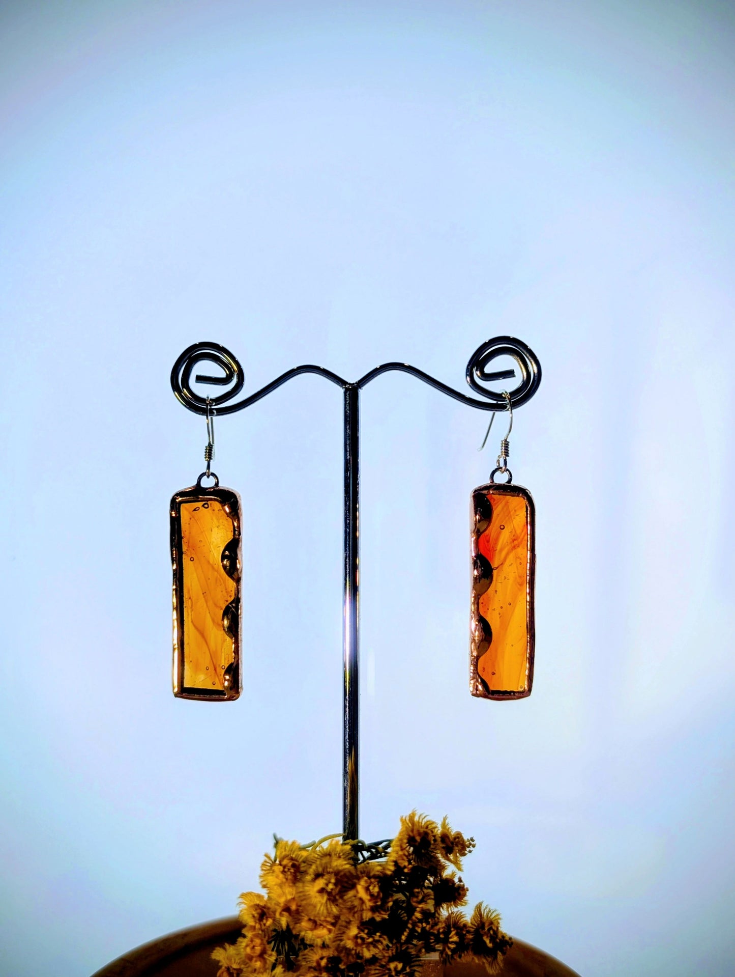 Pair of amber-colored earrings on a metal stand against a blue background