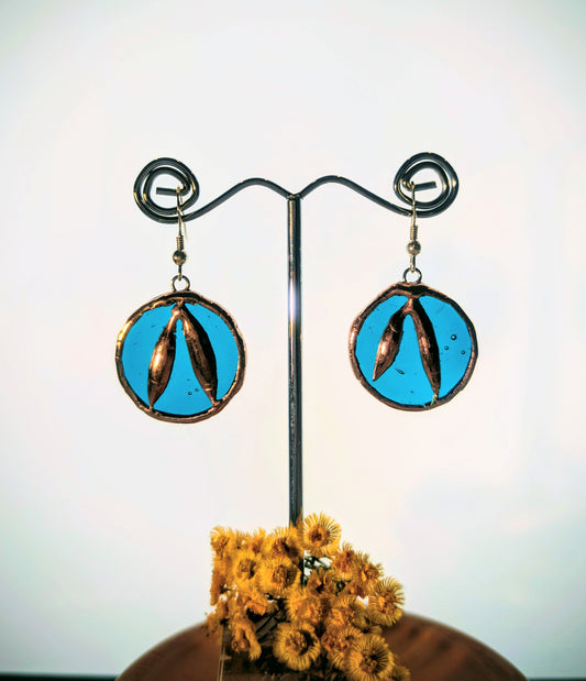 Pair of earrings with blue circular design on a stand with dried flowers.
