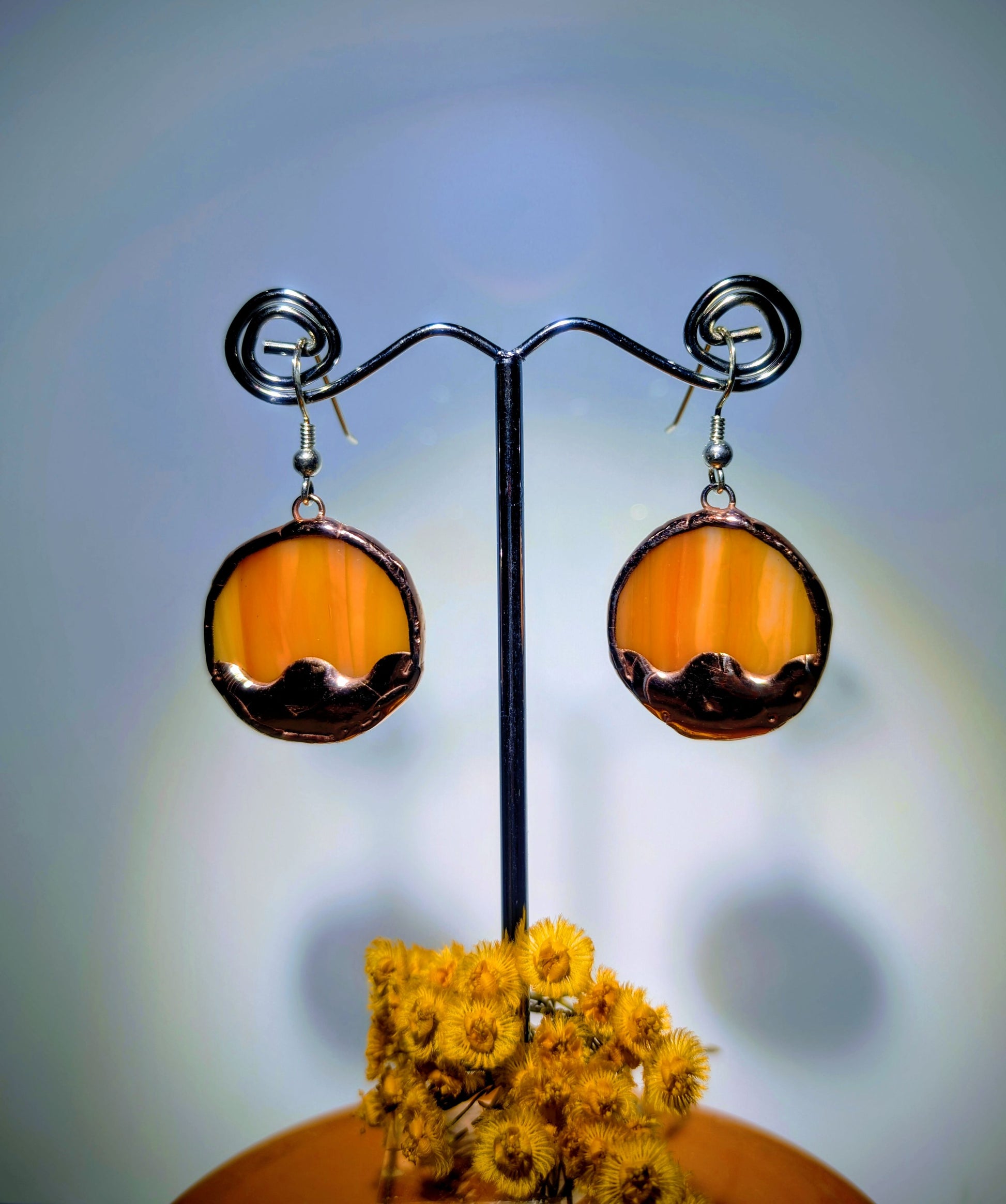 Pair of amber-colored earrings on a stand with a blurred background