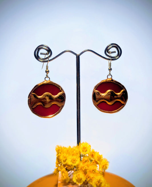 Pair of red and gold earrings on a stand with yellow flowers in the foreground.