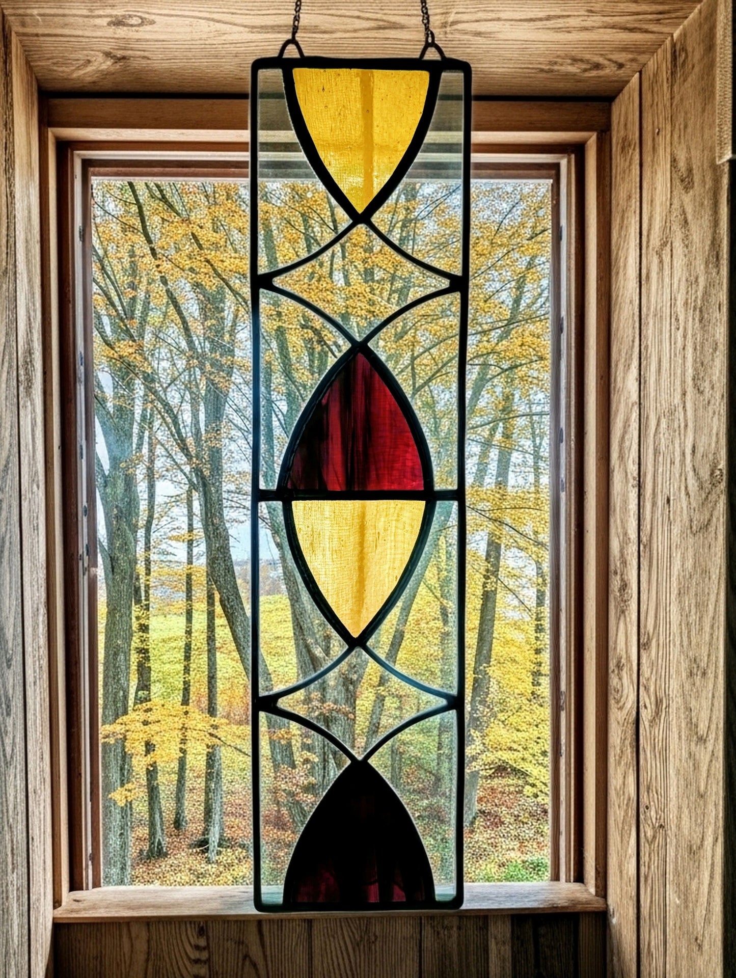 Stained glass panel with geometric design in front of a window with a view of trees.