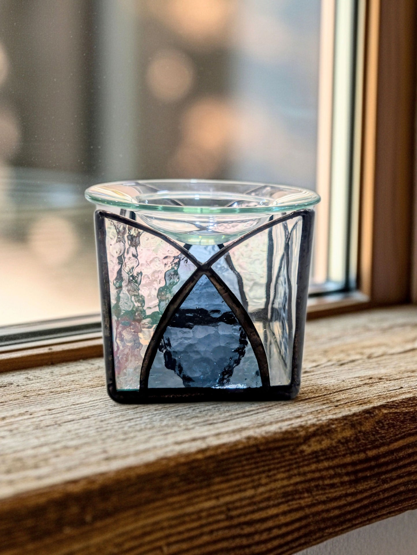Glass candle holder with decorative design on a wooden surface near a window