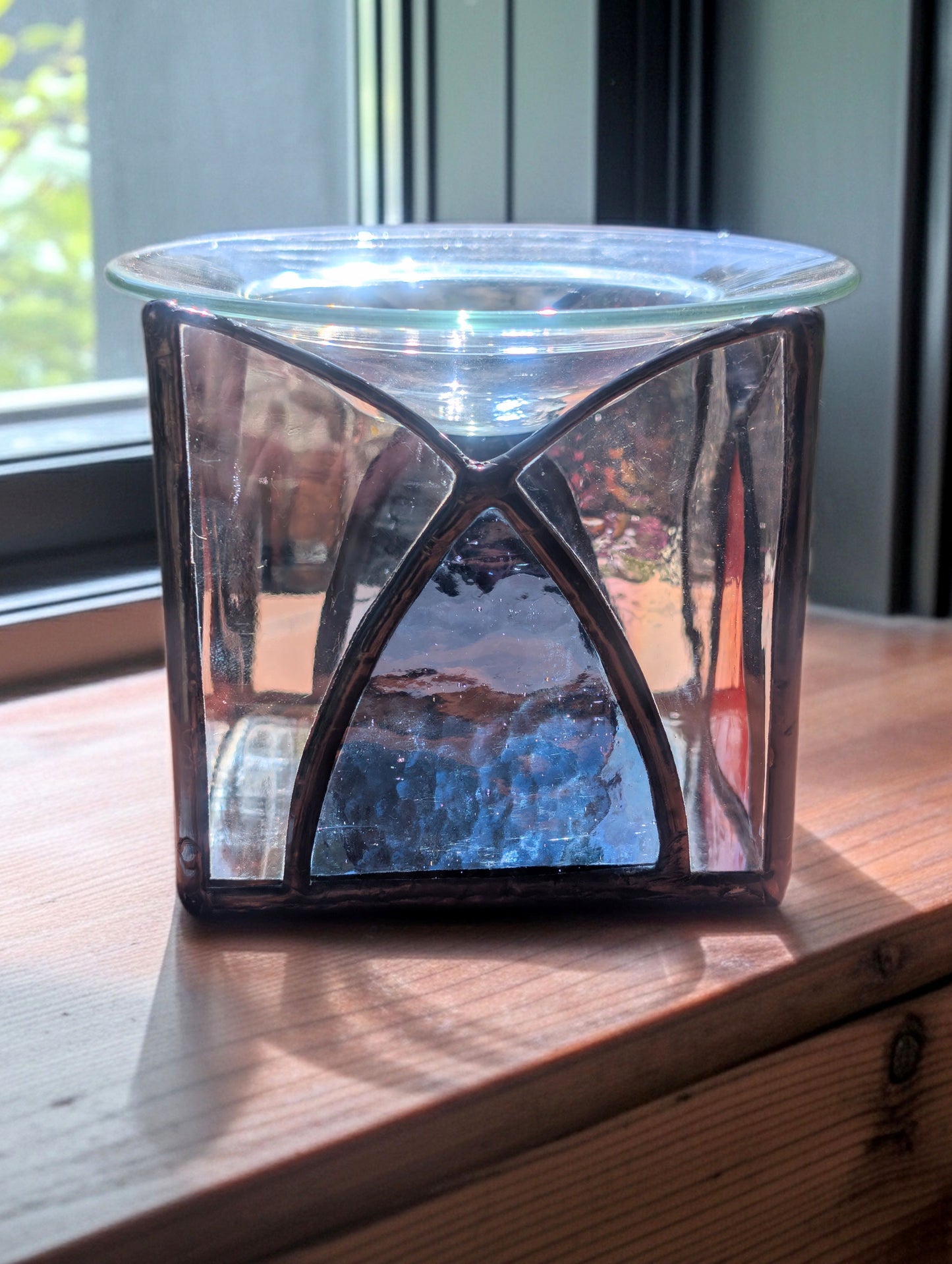 Hexagonal glass candle holder on a wooden surface with a window in the background