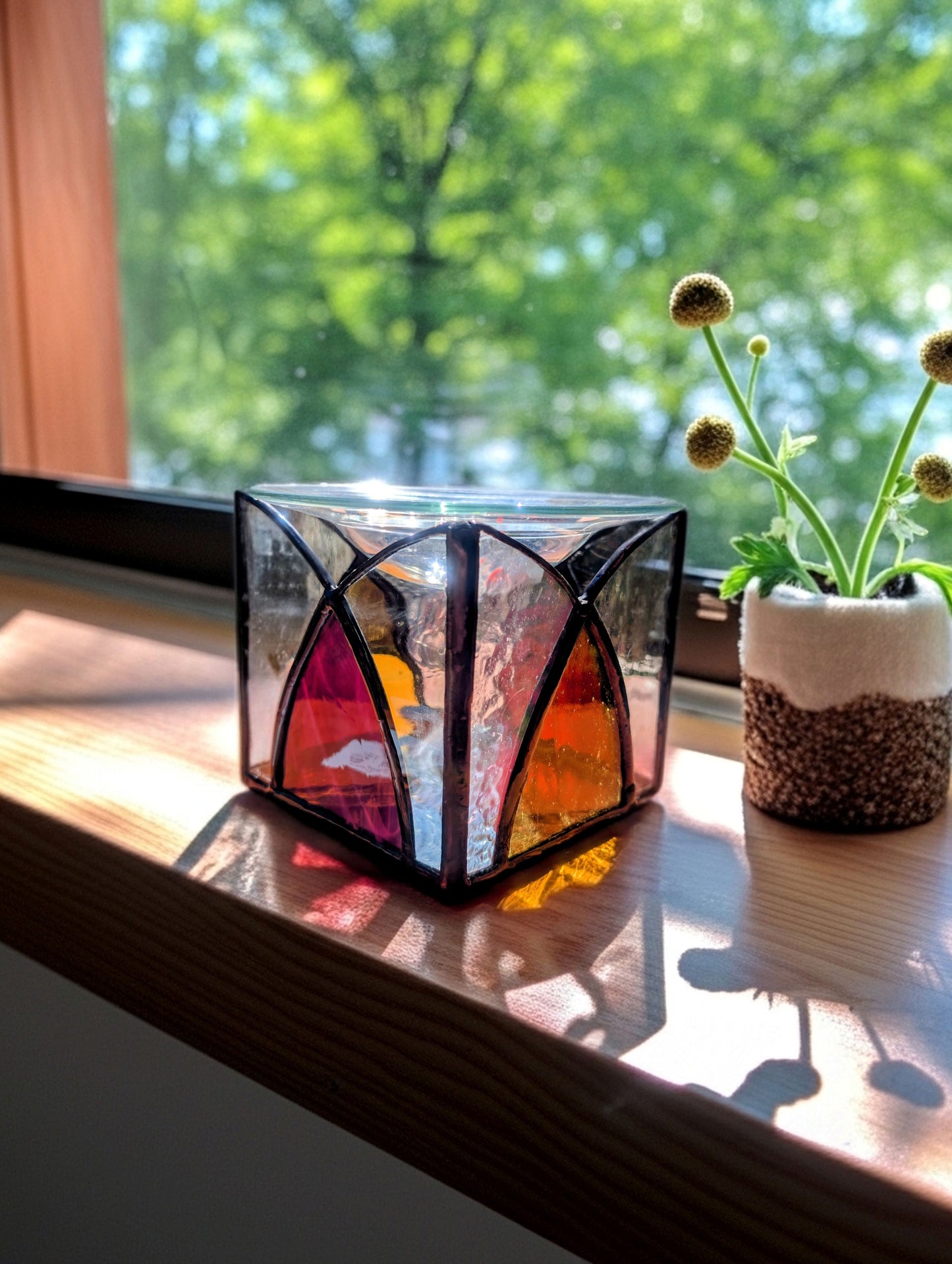 Colorful geometric candle holder on a windowsill with a plant in the background