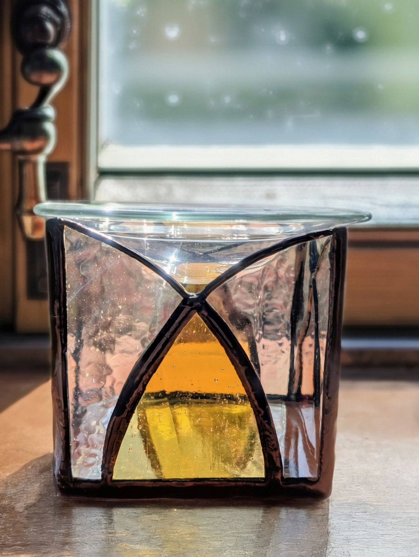 Decorative glass candle holder with a warm glow on a wooden surface.